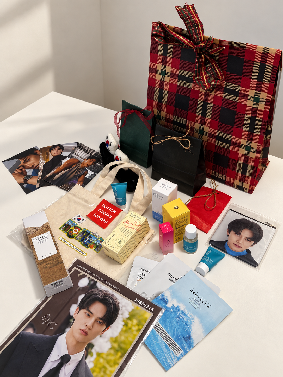 Prodotti skincare coreani, photocard e gadget del calendario dell'avvento K-Dream disposti davanti al sacchetto regalo scozzese