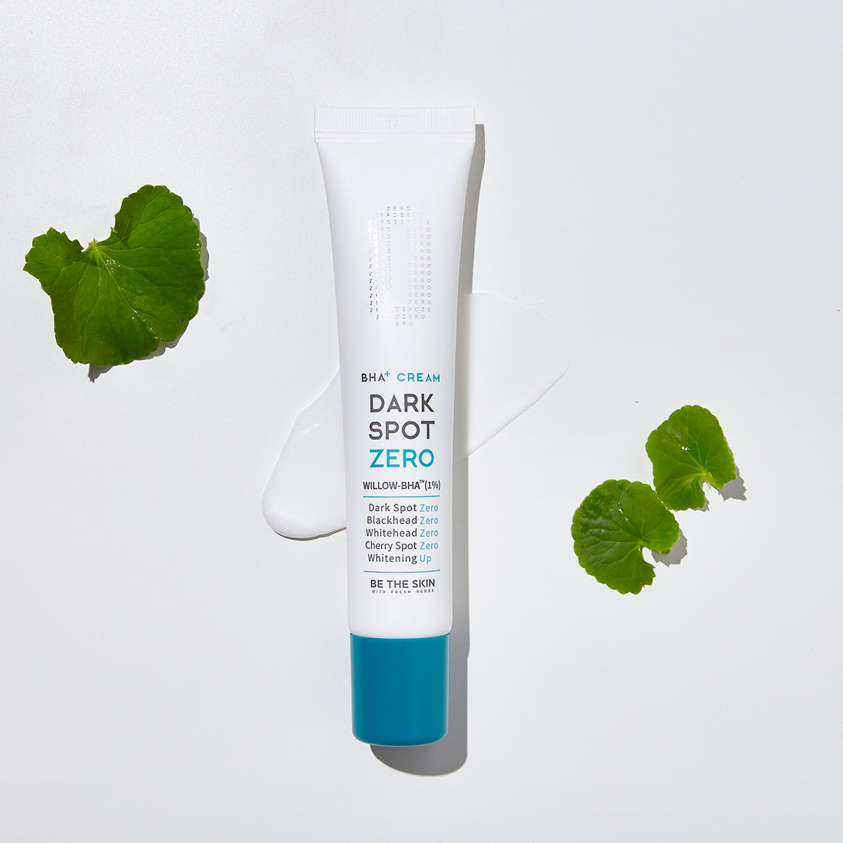 Tubo della crema BE THE SKIN Dark Spot Zero BHA+ con tappo azzurro, posizionato su uno sfondo bianco con crema sparsa e foglie di Centella Asiatica ai lati.
