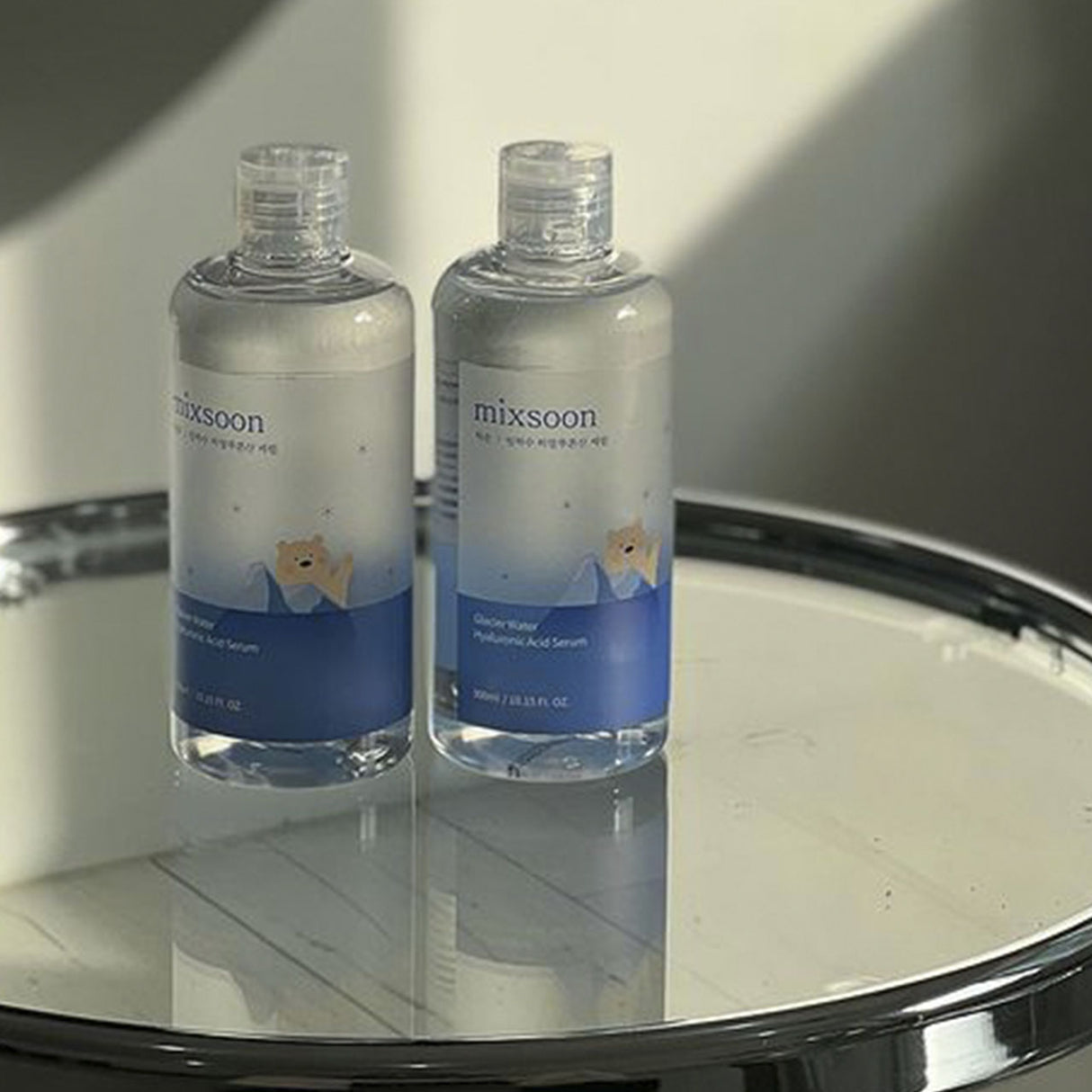 Flacone di Mixsoon Glacier Water Hyaluronic Acid Serum avvolto da schizzi d'acqua trasparente su sfondo azzurro chiaro, che trasmette una sensazione di freschezza e idratazione intensa.