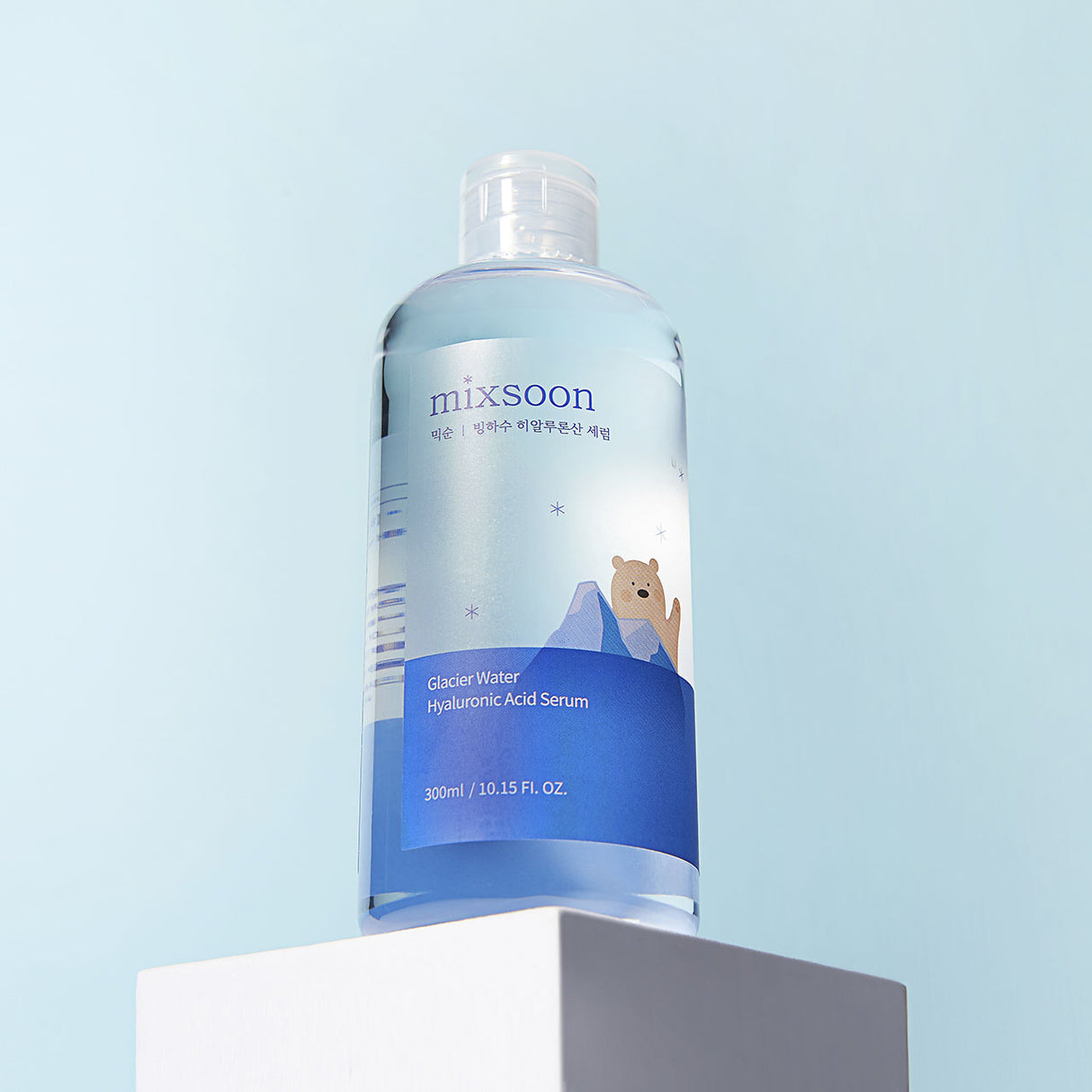Flacone trasparente di Mixsoon Glacier Water Hyaluronic Acid Serum da 300 ml, posizionato su un piedistallo bianco con sfondo azzurro chiaro. L’etichetta del prodotto mostra un orso polare illustrato tra montagne ghiacciate, evocando freschezza e idratazione glaciale.