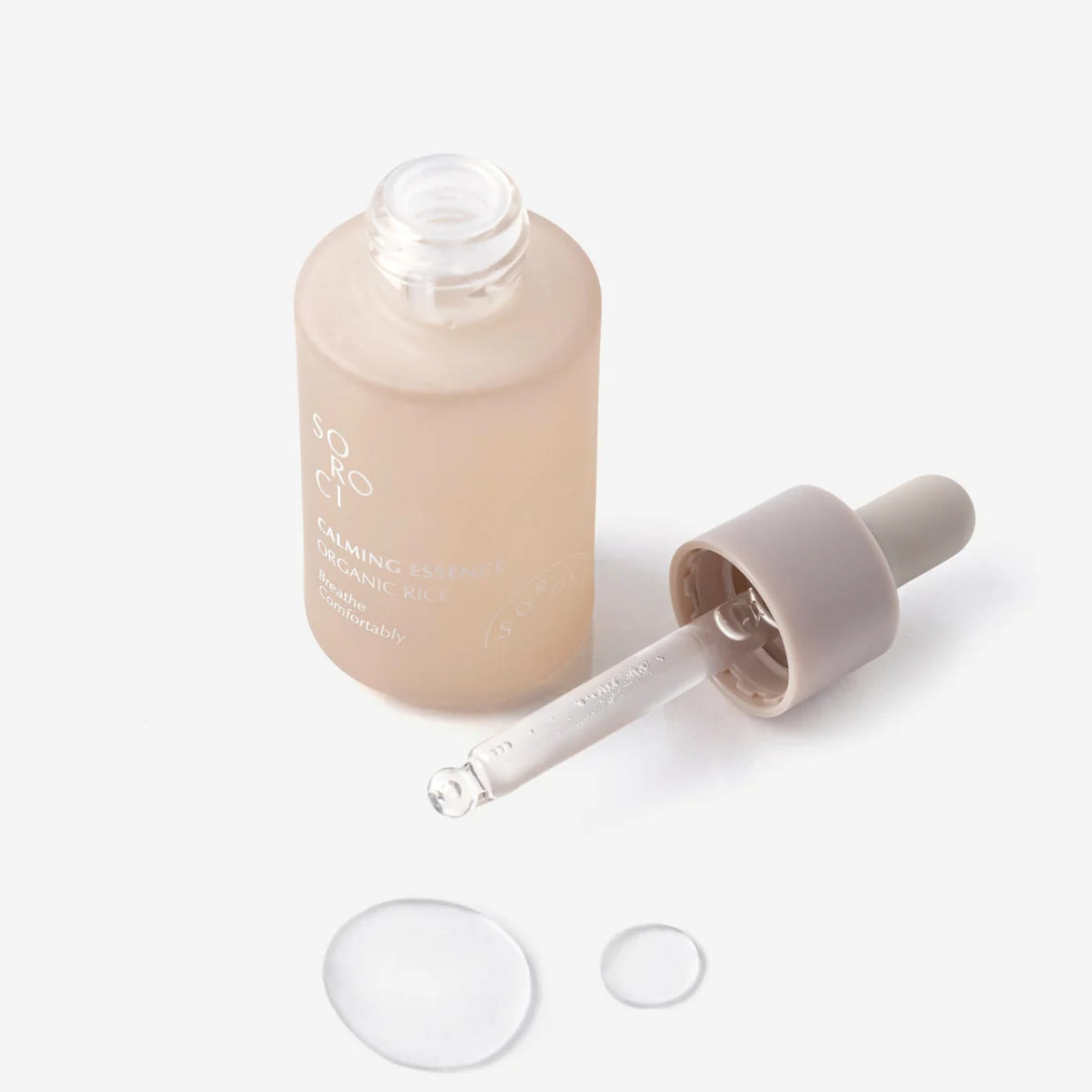 Flacone aperto di SOROCI Calming Essence Organic Rice con pipetta appoggiata accanto e gocce di prodotto trasparente su sfondo bianco.