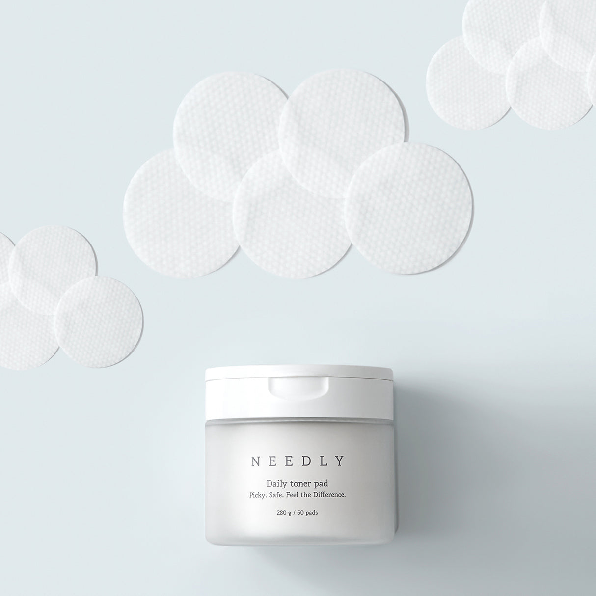 Vasetto del prodotto "NEEDLY Daily Toner Pad" in primo piano su sfondo azzurro chiaro, circondato da numerosi dischetti tonificanti bianchi con texture a nido d'ape, disposti artisticamente intorno.