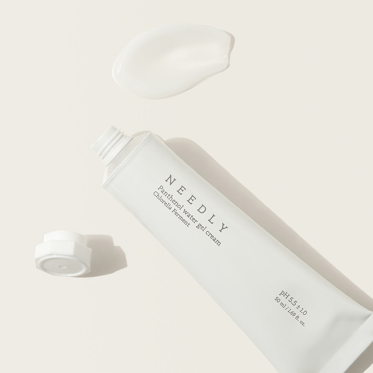 Tubo bianco aperto della Needly Panthenol Water Gel Cream su sfondo beige, con tappo staccato e una noce di crema bianca visibile sopra, in una composizione luminosa e minimalista.