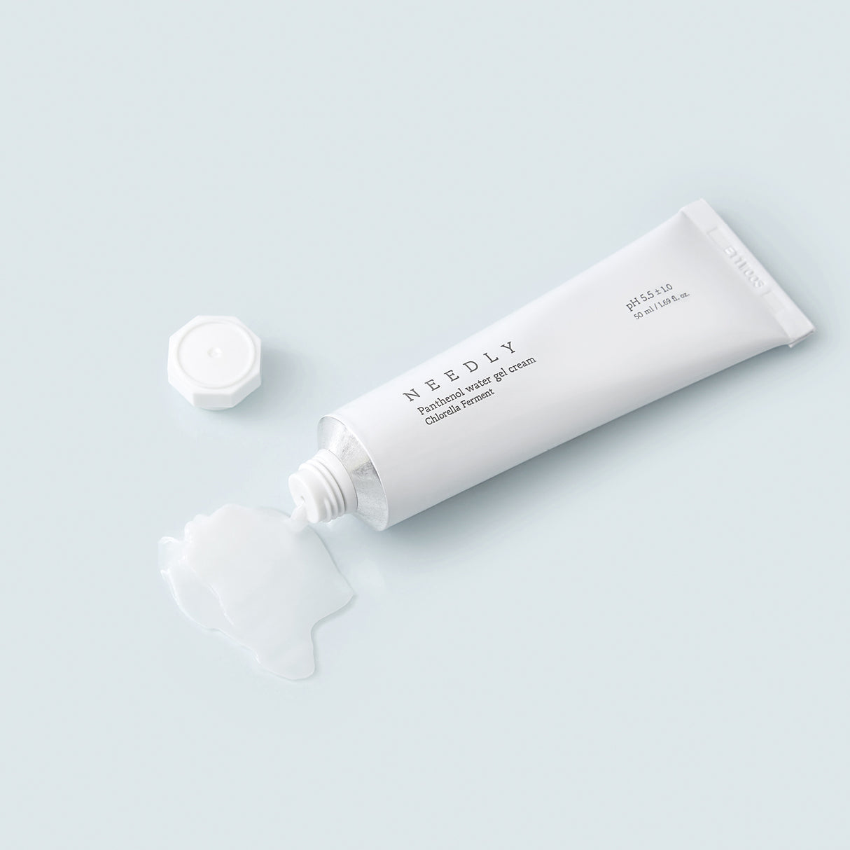 Un tubetto bianco di Needly Panthenol Water Gel Cream con tappo svitato e crema trasparente-gel fuoriuscita su una superficie azzurra, mostrata in un contesto minimal e fresco