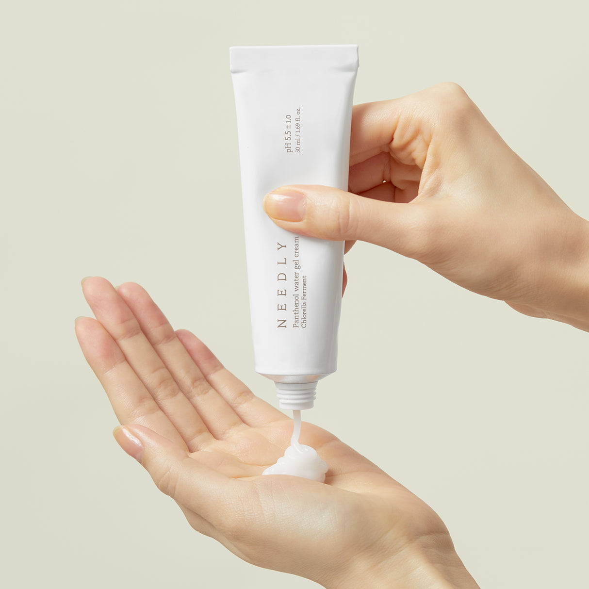 Due mani che mostrano l'applicazione di Needly Panthenol Water Gel Cream, mentre il gel bianco viene spremuto dal tubo nella mano aperta, su sfondo beige chiaro
