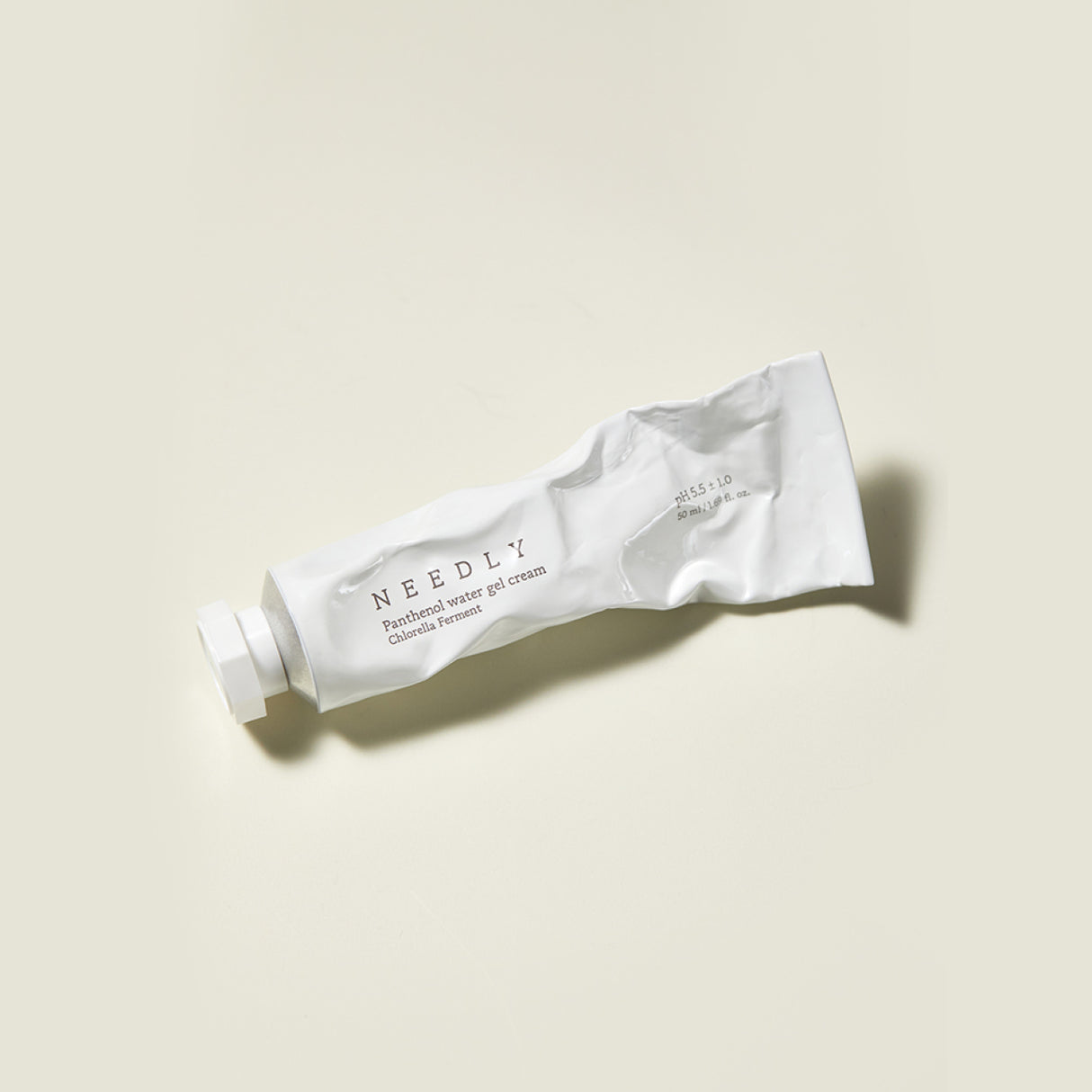 Il tubo bianco leggermente schiacciato della Needly Panthenol Water Gel Cream è appoggiato su una superficie beige chiaro, con tappo chiuso e ombra laterale visibile.
