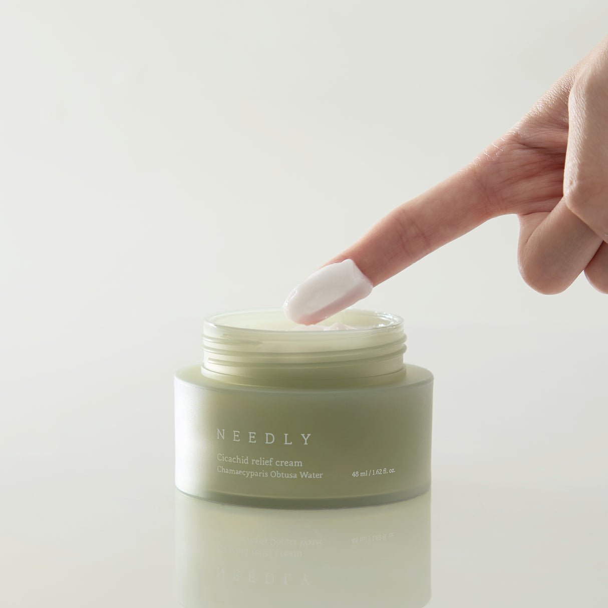 Crema viso Needly Cicachid Relief Cream da 48 ml con Chamaecyparis Obtusa Water, texture cremosa rosata applicata con un dito, su sfondo bianco minimalista.