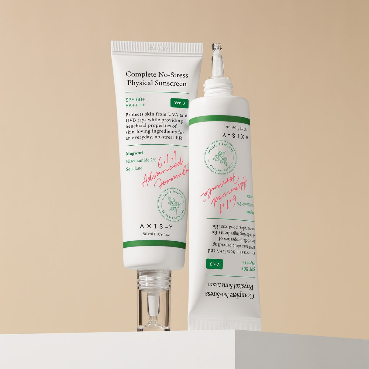 Due tubetti di crema solare AXIS-Y Complete No-Stress SPF 50+ PA++++, uno in posizione verticale e l’altro inclinato, entrambi con etichette visibili su sfondo beige chiaro.