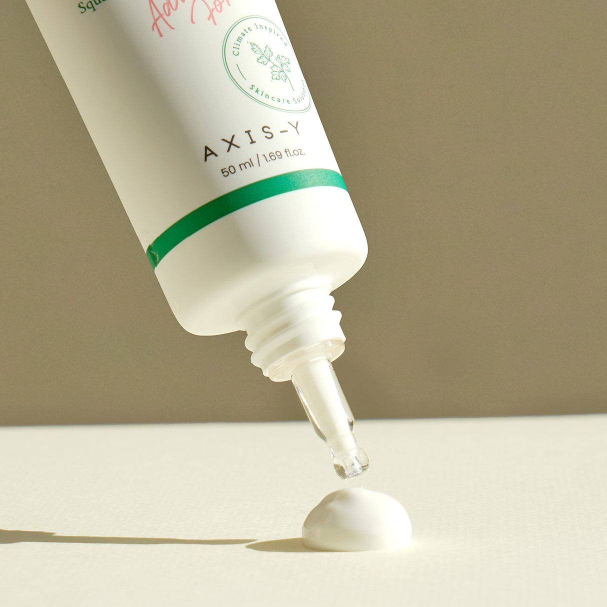 Tubetto di crema solare AXIS-Y inclinato con beccuccio aperto, una goccia di prodotto che cade formando una piccola quantità di crema su sfondo neutro.