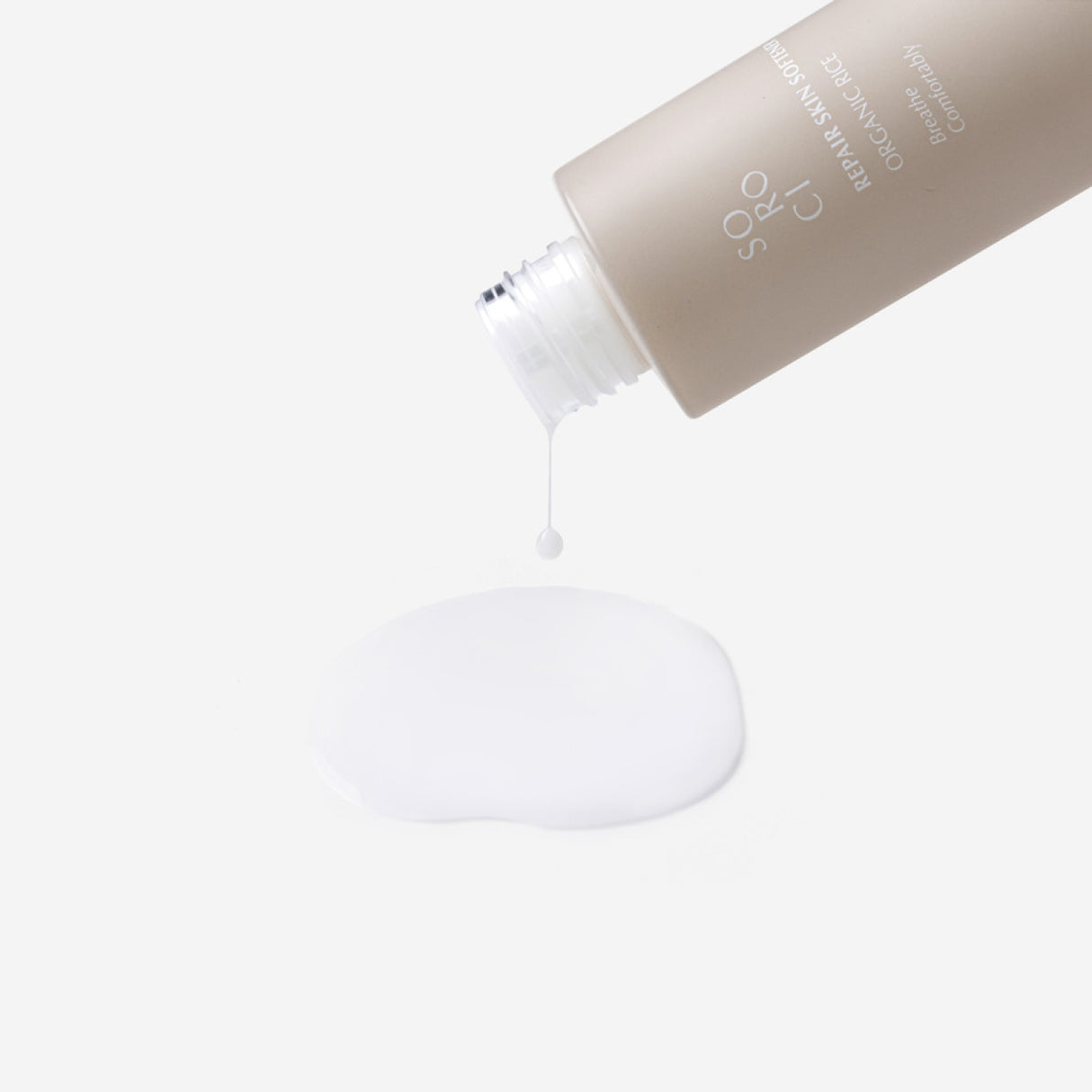 Close-up del flacone inclinato di SOROCI Repair Skin Softener Organic Rice mentre una goccia di prodotto lattiginoso cade, formando una pozza su sfondo bianco.