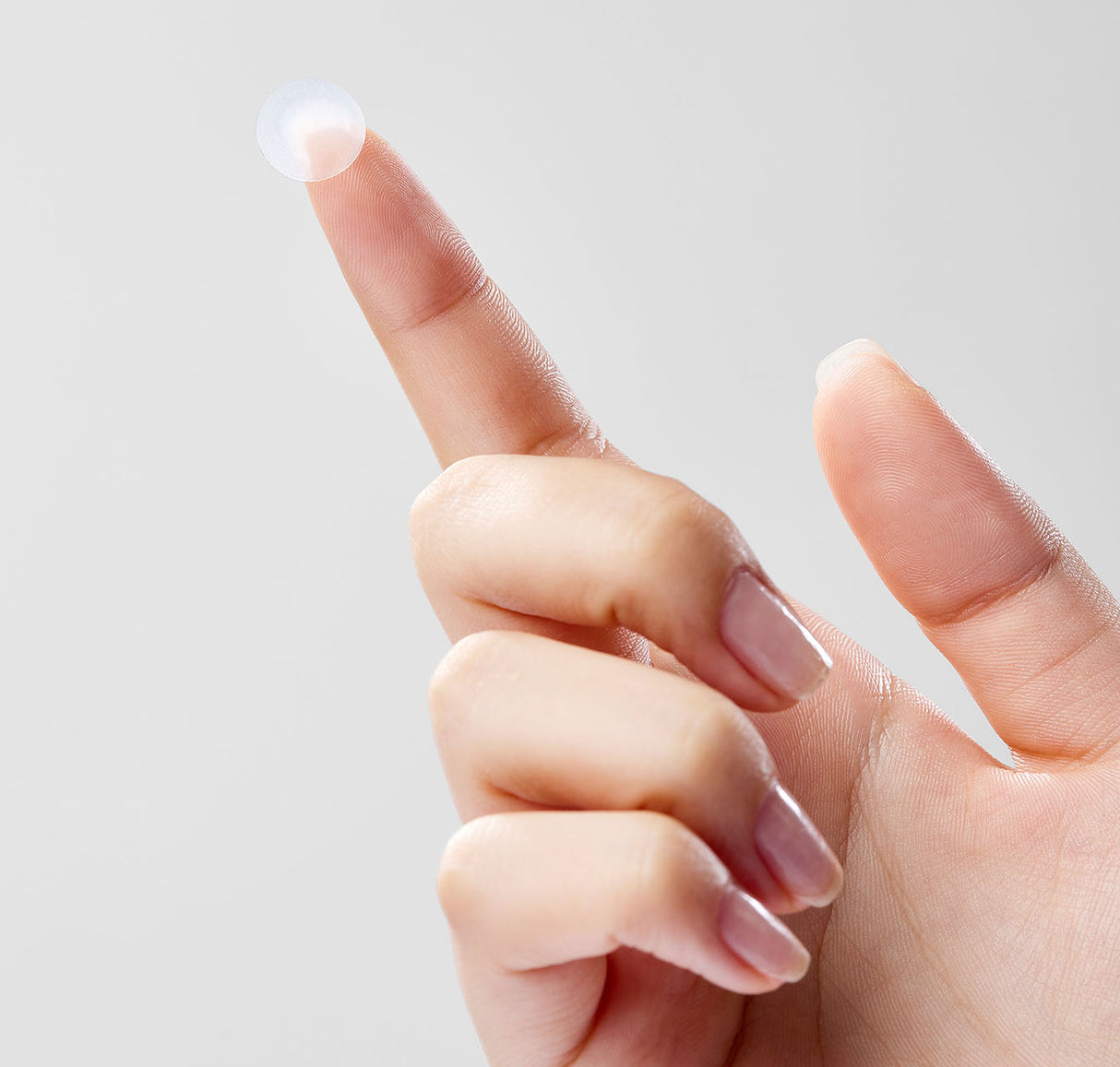 Primo piano di una mano che tiene un cerotto trasparente Mixsoon Spot Cleancare Patch sulla punta del dito indice, su sfondo grigio chiaro.