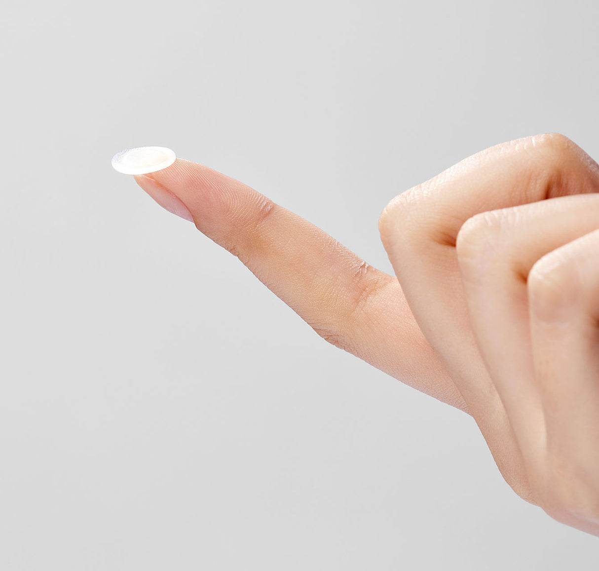 Primo piano di una mano che tiene un cerotto Mixsoon Spot Cleancare Patch sulla punta del dito indice, su sfondo grigio chiaro.