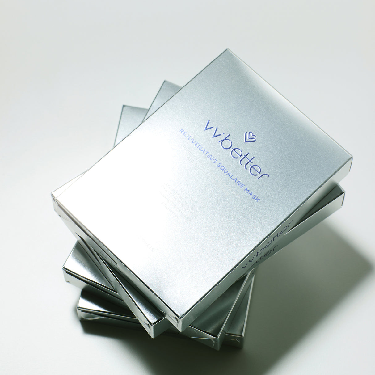 Confezioni argentate impilate della maschera viso vvbetter Rejuvenating Squalane Mask, fotografate su sfondo chiaro con luce naturale.