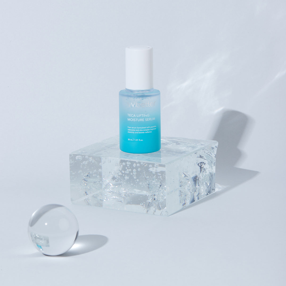 Flacone azzurro del siero viso Wbetter TECA Lifting Moisture da 30ml posizionato su un blocco trasparente tipo ghiaccio, con sfera decorativa su sfondo chiaro