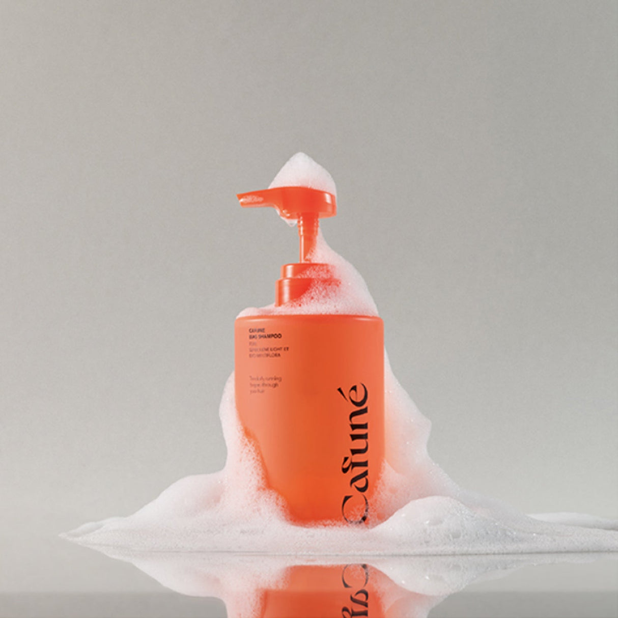 Flacone shampoo Cafuné arancione con dispenser ricoperto di schiuma, visual che rappresenta la detersione profonda e delicata del cuoio capelluto.
