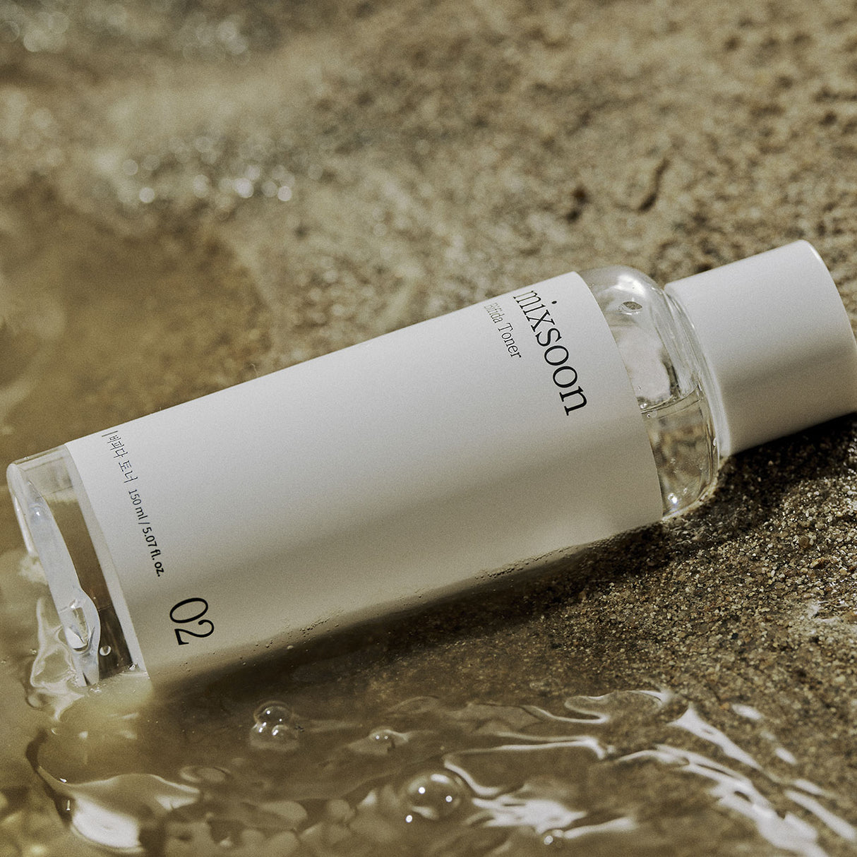 Mixsoon Centella Asiatica toner flacone trasparente con etichetta bianca su sabbia con acqua