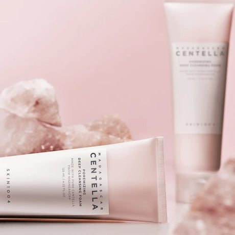 Tubo da 125ml del detergente SKIN1004 Madagascar Centella Poreminizing Deep Cleansing Foam con una dose di prodotto schiumoso sulla parte superiore, su sfondo rosa perlato.