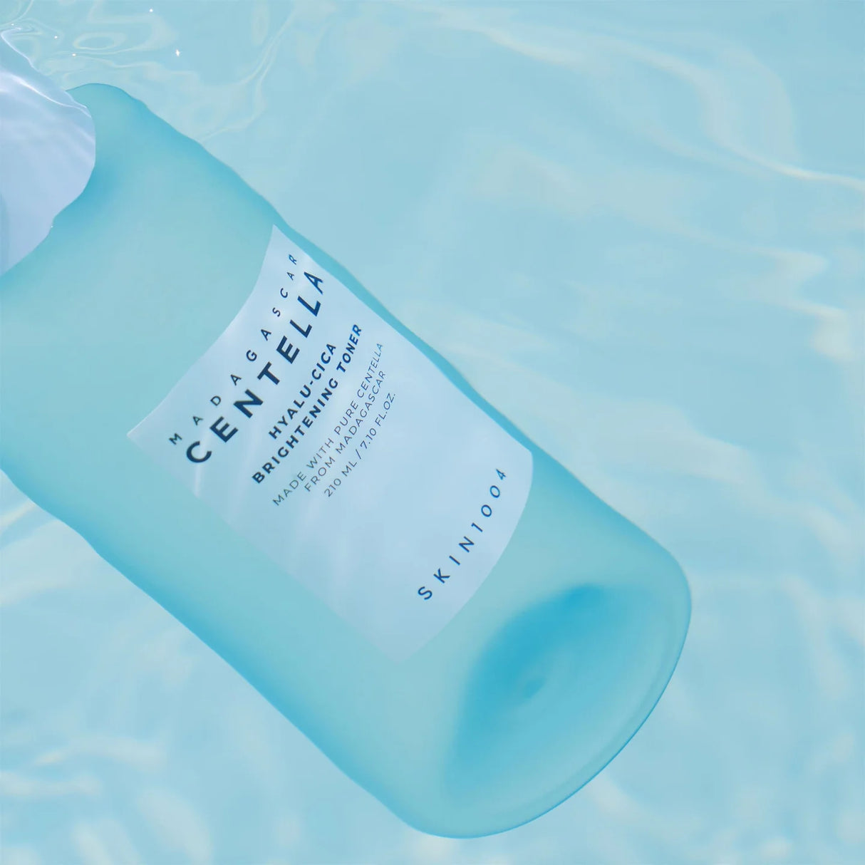 Flacone azzurro del tonico viso SKIN1004 Centella Hyalu-Cica Brightening da 210ml immerso in acqua, con etichetta bianca su sfondo acquatico