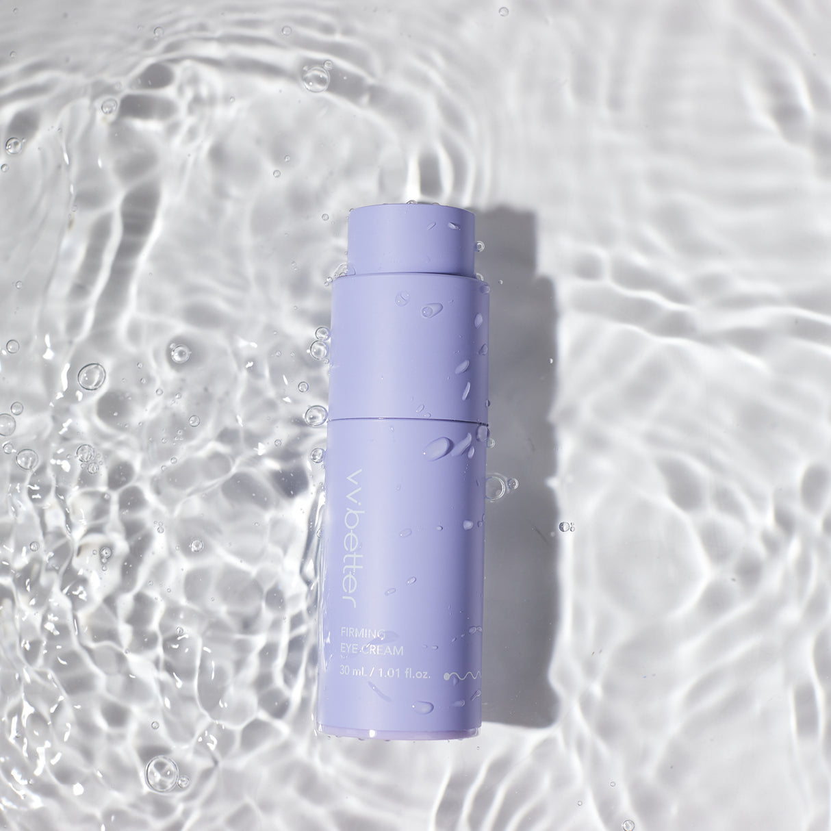 Flacone color lavanda del vvbetter Firming Eye Cream da 30 ml / 1.01 fl.oz., adagiato su una superficie d’acqua con riflessi e gocce visibili, evocando una sensazione di freschezza e idratazione.