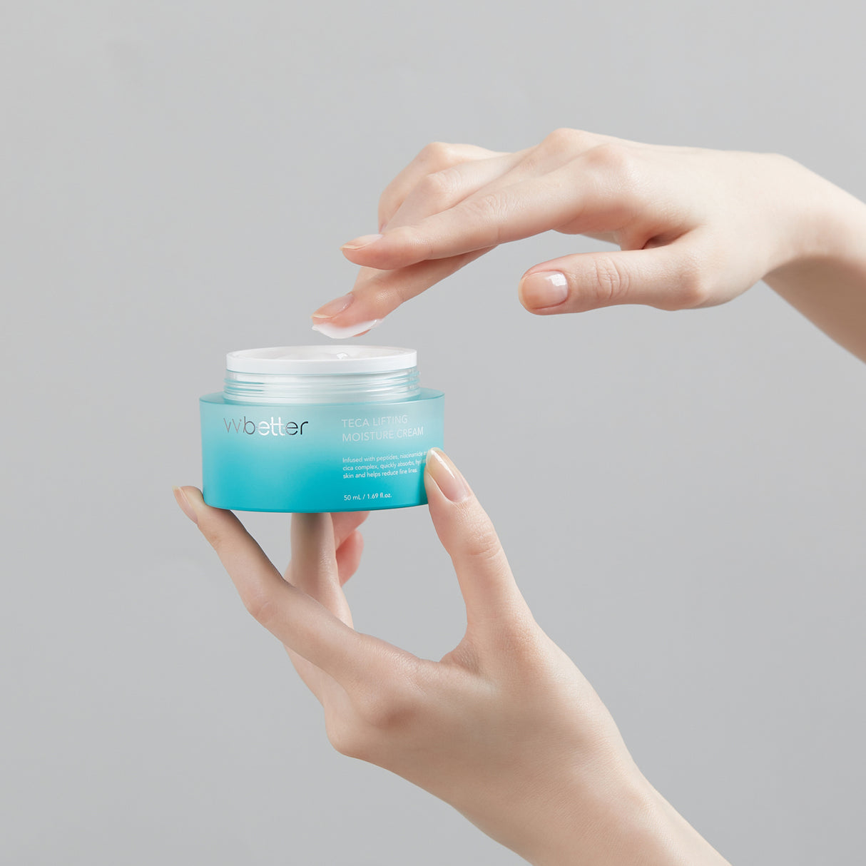 Una mano apre un vasetto azzurro della vvbetter Teca Lifting Moisture Cream da 50 ml, mentre l'altra preleva una piccola quantità di crema bianca. Sullo sfondo neutro grigio, il packaging risalta con le sue scritte bianche che evidenziano gli ingredienti idratanti e anti-età.