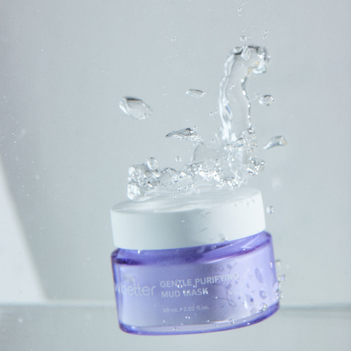 Barattolo lilla della vvbetter Gentle Purifying Mud Mask immerso nell’acqua con uno splash dinamico. Le gocce e i flussi d’acqua sospesi accentuano la freschezza e la vitalità del prodotto, creando un effetto visivo rinfrescante e pulito.