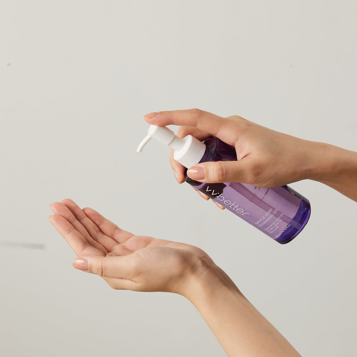 Due mani femminili utilizzano il flacone del vvbetter Gentle Deep Cleansing Oil, premendo il dispenser bianco per erogare il prodotto su una mano aperta, su sfondo neutro chiaro.
