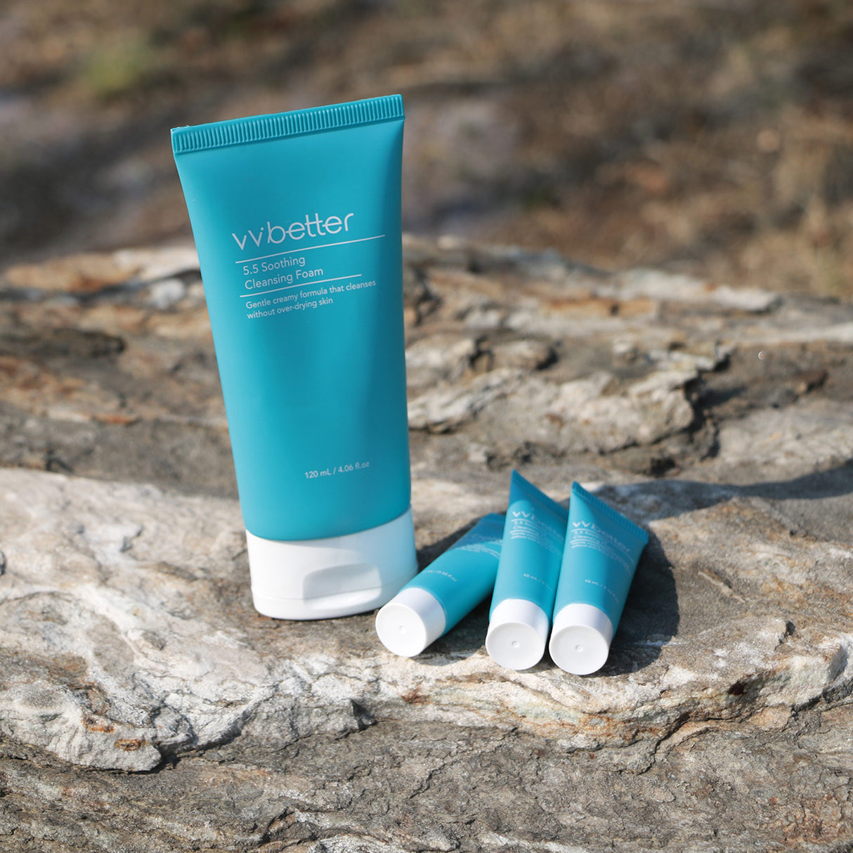 Un tubo grande e tre tubetti piccoli del vvbetter 5.5 Soothing Cleansing Foam posizionati su una superficie rocciosa all'aperto, tutti di colore azzurro con tappo bianco e scritte bianche