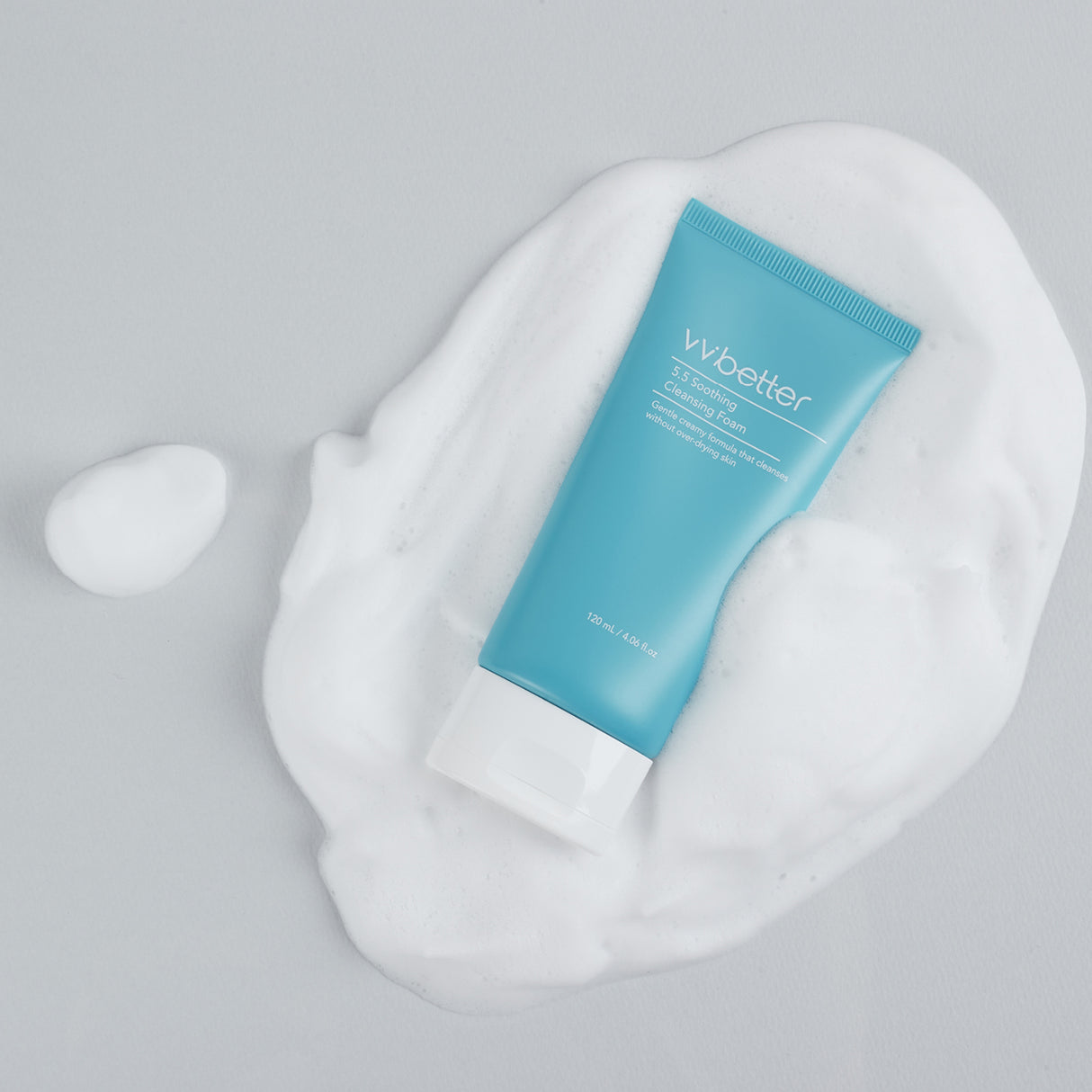 Tubo del vvbetter 5.5 Soothing Cleansing Foam azzurro con tappo bianco adagiato sopra una generosa quantità di schiuma bianca su sfondo grigio chiaro, suggerendo la consistenza cremosa e soffice del prodotto.