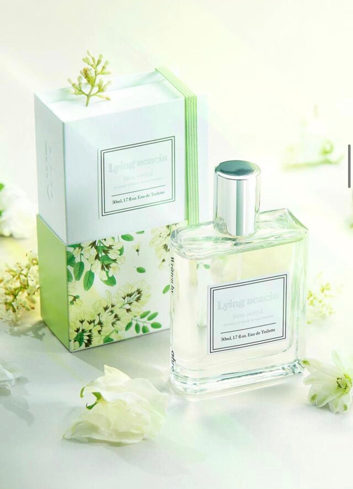 Flacone del profumo coreano Ahro Lying Acacia Eau de Toilette 50 ml con confezione illustrata floreale verde e bianca, fotografato su sfondo chiaro con fiori bianchi decorativi.