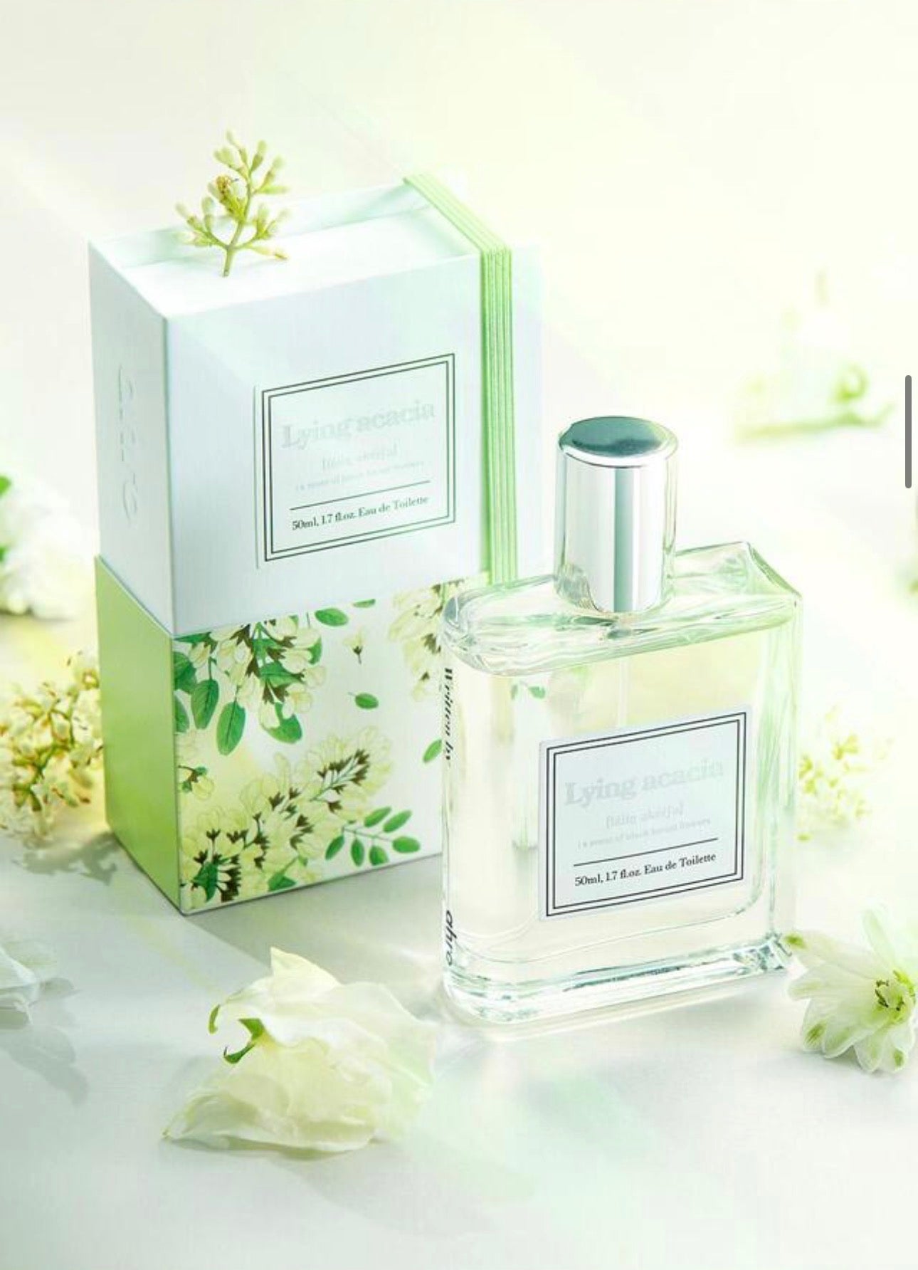 Flacone del profumo coreano Ahro Lying Acacia Eau de Toilette 50 ml con confezione illustrata floreale verde e bianca, fotografato su sfondo chiaro con fiori bianchi decorativi.