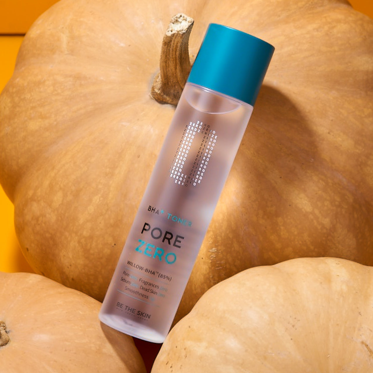 Flacone del tonico BE THE SKIN Pore Zero BHA+ appoggiato su zucche arancioni, con sfondo caldo e autunnale, che crea contrasto tra freschezza e stagionalità.