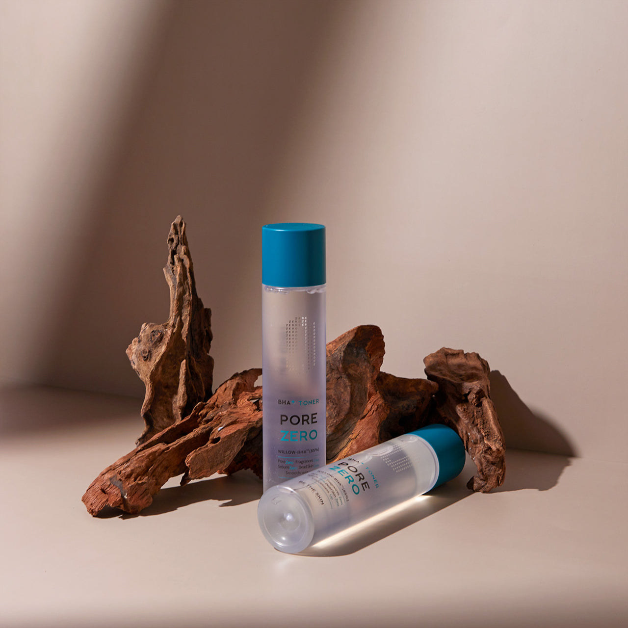 Due flaconi di toner Pore Zero BHA+ Toner di Be The Skin posizionati accanto a pezzi di legno decorativi su una superficie beige, con luce calda e ombre morbide a creare un effetto naturale ed elegante.