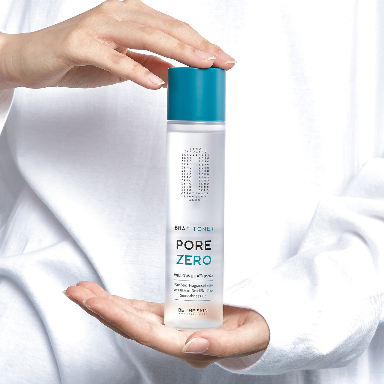 
Mani che tengono e mostrano il toner Pore Zero BHA+ Toner di Be The Skin, flacone trasparente con tappo blu su sfondo bianco.
