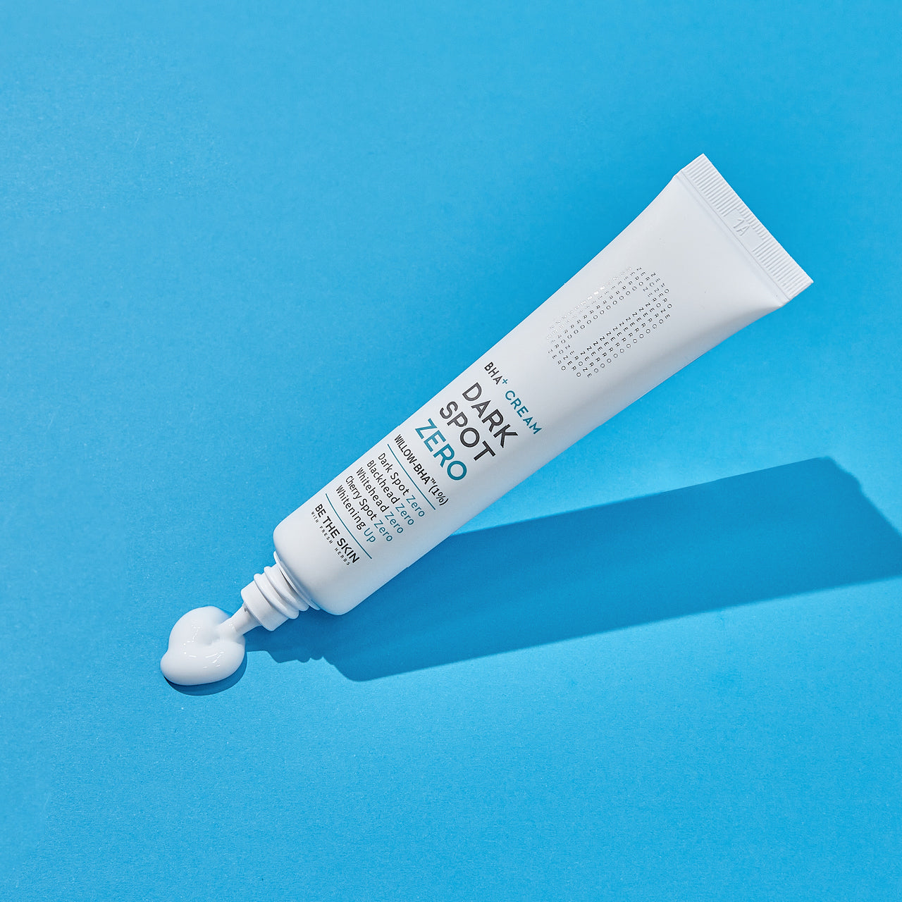 Tubo di crema BE THE SKIN Dark Spot Zero BHA+ su sfondo azzurro, con il prodotto visibile fuoriuscito a forma di cuore sulla superficie.