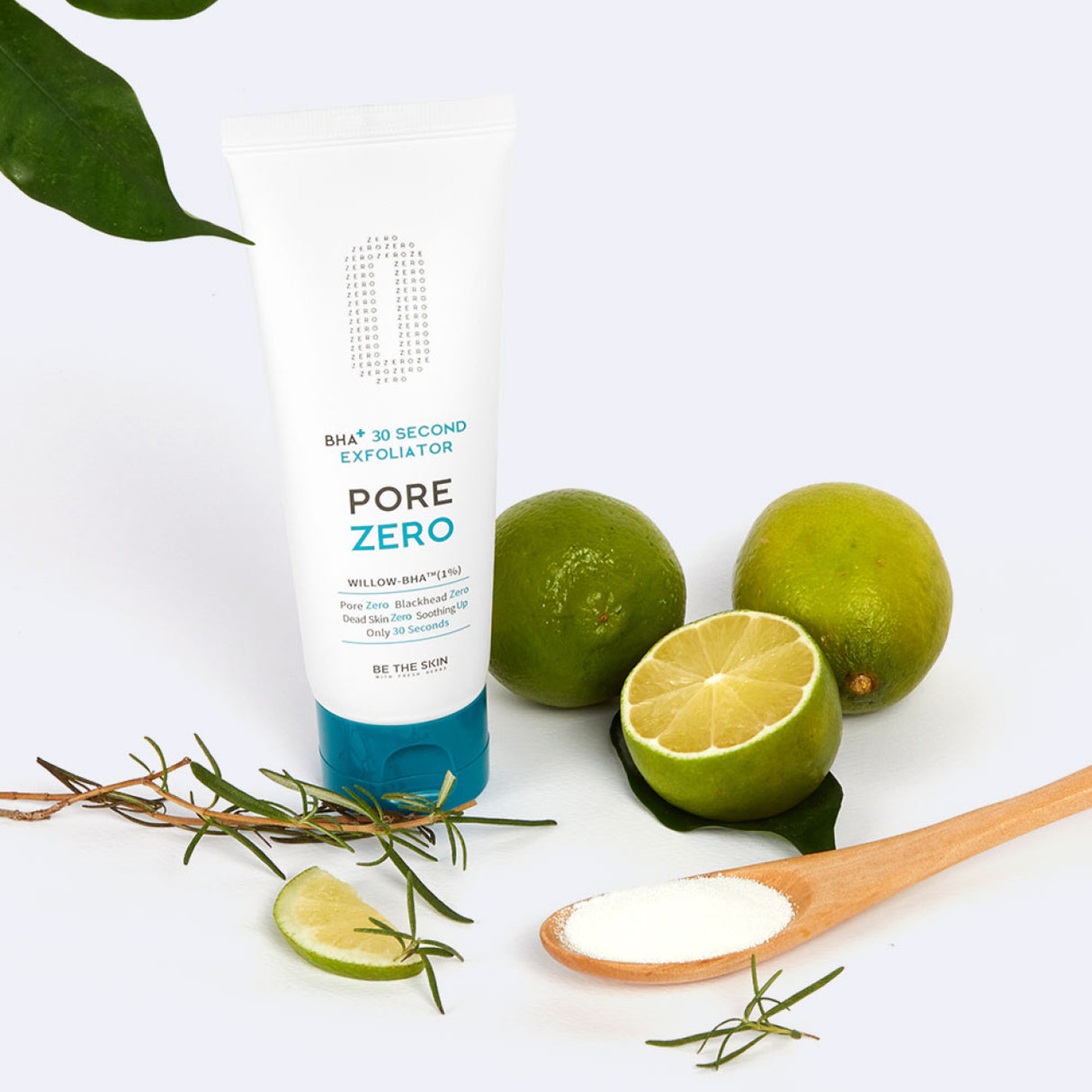 Tubo dell’esfoliante BE THE SKIN PORE ZERO BHA+ 30 Second Exfoliator posizionato accanto a lime interi e tagliati, rametti di rosmarino e un cucchiaio di legno con polvere bianca, su sfondo bianco chiaro.

