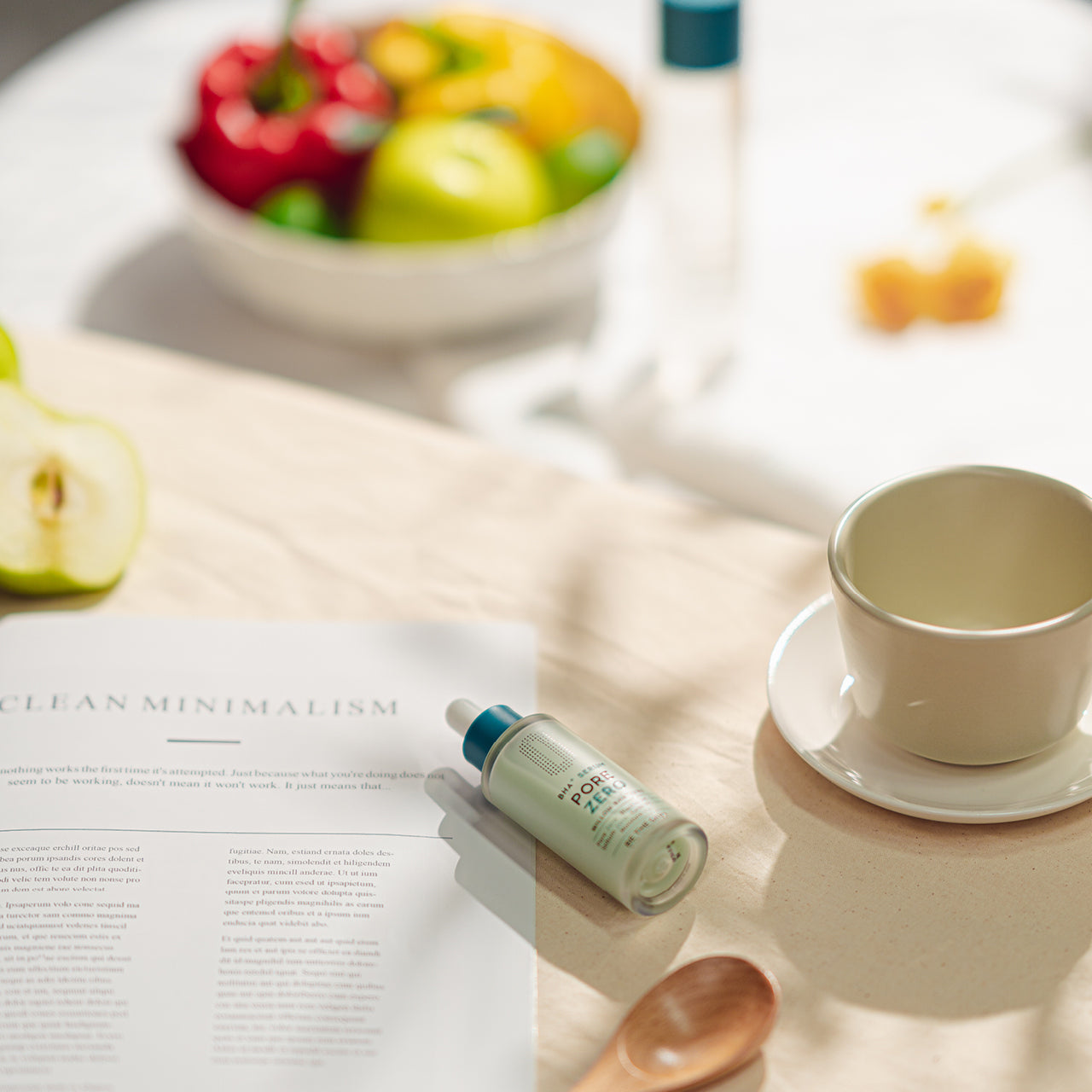 Flacone del siero BE THE SKIN PORE ZERO BHA+ appoggiato su una tavola da colazione, accanto a una tazza, una rivista e frutta fresca, in un'atmosfera luminosa e minimalista.