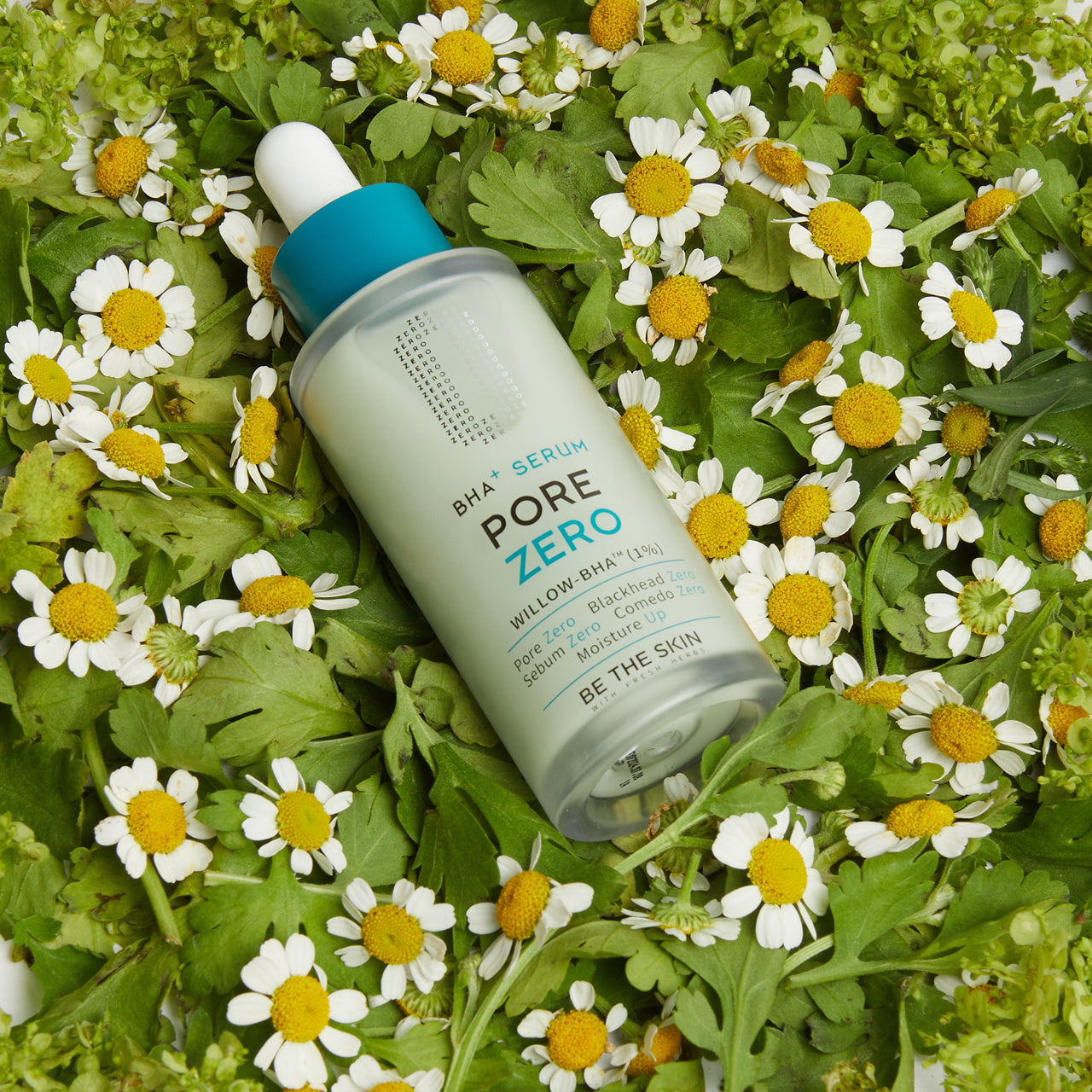 Flacone del siero BE THE SKIN PORE ZERO BHA+ adagiato su un letto di margherite e foglie verdi, con tappo blu e scritte nere e azzurre.

