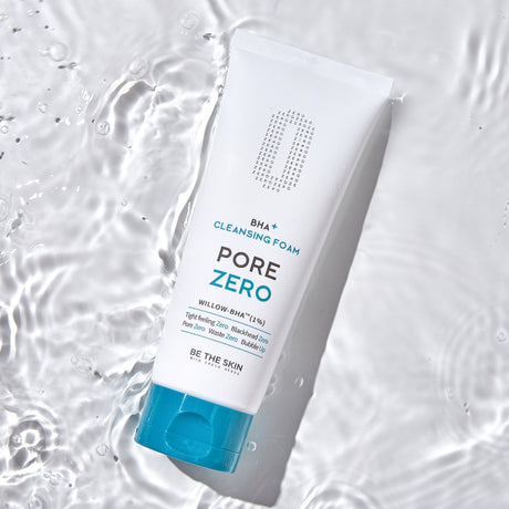 Detergente viso BE THE SKIN PORE ZERO BHA+ CLEANSING FOAM posato su superficie bagnata con giochi d’acqua trasparente.