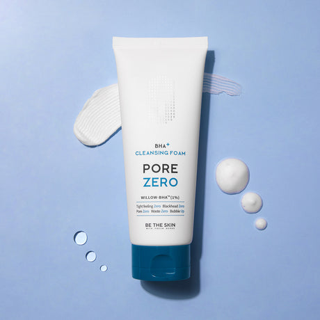 Detergente viso BE THE SKIN PORE ZERO BHA+ CLEANSING FOAM su sfondo azzurro, con tracce di prodotto e bolle schiumose accanto al flacone.

