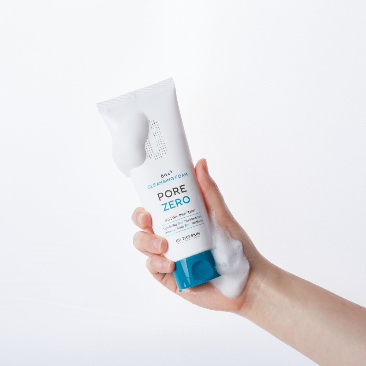 Mano che tiene il detergente viso BE THE SKIN PORE ZERO BHA+ CLEANSING FOAM, ricoperto da schiuma bianca, su sfondo chiaro.

