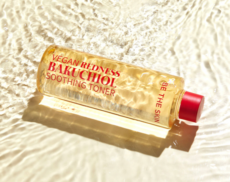 vegan redness bakuchiol soothing toner barattolo trasparente con linquido giallo su sfondo sabbia con acqua