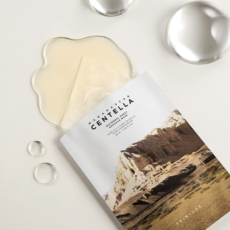Confezione SKIN1004 Madagascar Centella Watergel Sheet Ampoule Mask aperta con fuoriuscita di prodotto e gocce fotografata su base chiara
