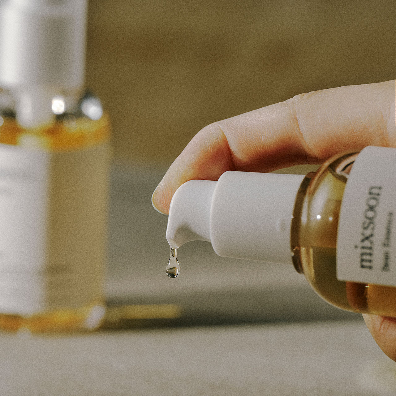 Mano che eroga la Mixsoon Bifida Essence con dispenser a pompa, mostrando una goccia del prodotto e il flacone minimalista.