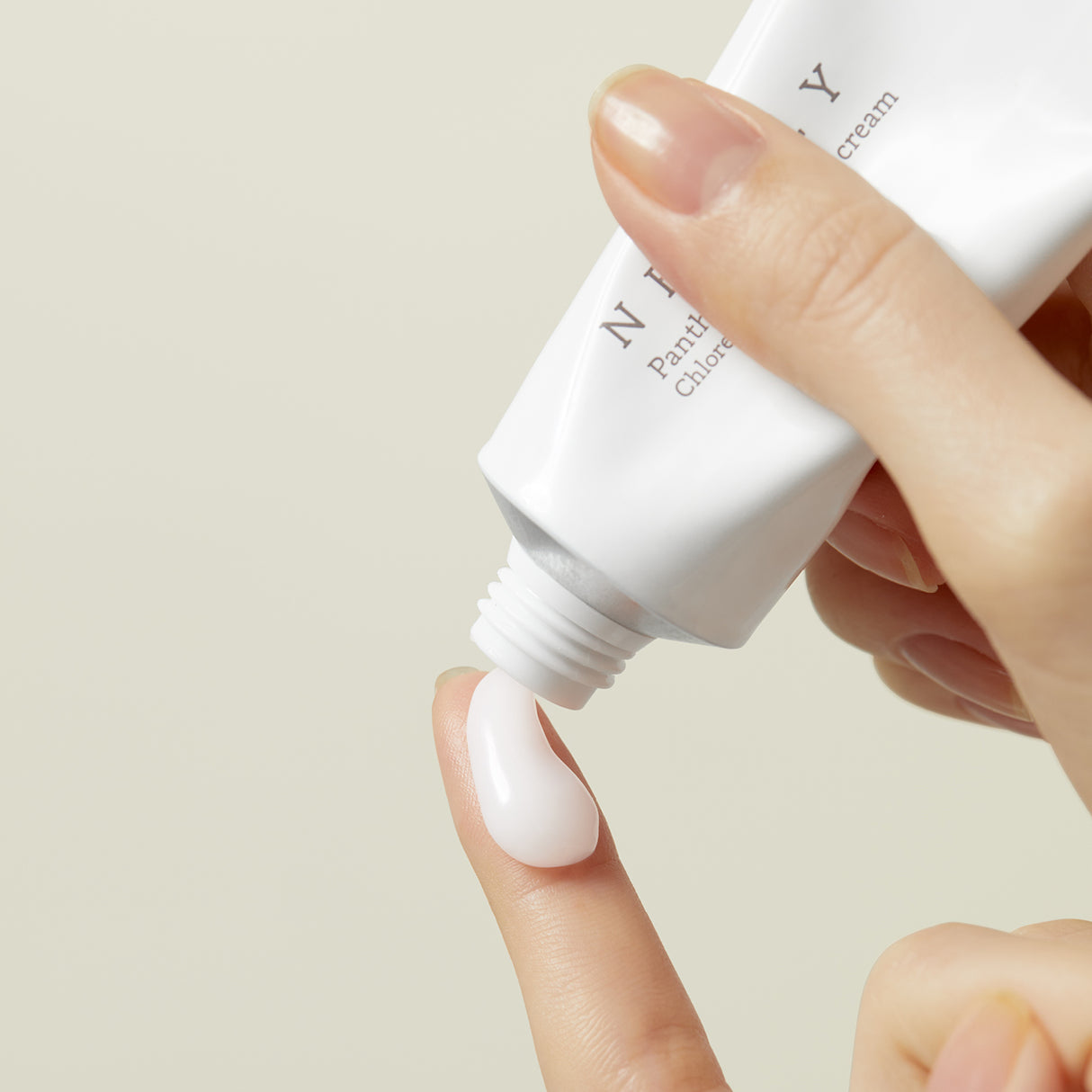 Una mano che applica Needly Panthenol Water Gel Cream sul dito, mostrando la texture cremosa e lattiginosa del prodotto mentre fuoriesce dal tubetto bianco.

