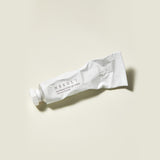 Il tubo bianco leggermente schiacciato della Needly Panthenol Water Gel Cream è appoggiato su una superficie beige chiaro, con tappo chiuso e ombra laterale visibile.

