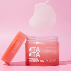 Barattolo di Vita Vita Raspberry PDRN Toner Pad Be The Skin aperto con dischetto imbevuto su sfondo rosa
