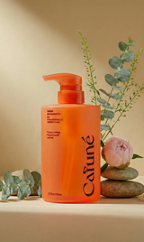 Bottiglia arancione con erogatore dello shampoo Cafuné Bias Shampoo 500 ml fotografata in set botanico con pietre decorative, foglie di eucalipto e fiore rosa su sfondo chiaro
