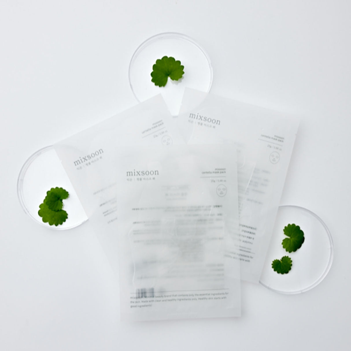 Maschere viso Mixsoon Centella Mask Pack disposte su sfondo bianco con foglie di centella asiatica in capsule di Petri, a richiamare l’origine naturale e l’efficacia lenitiva del prodotto.