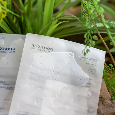 Confezione della Mixsoon Centella Mask Pack bagnata con gocce d'acqua, posizionata tra foglie verdi e ambientazione naturale, a sottolineare l’effetto rinfrescante e lenitivo del prodotto.