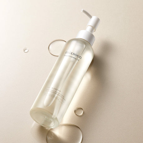 Flacone di Mixsoon Bean Cleansing Oil appoggiato su superficie chiara con gocce di olio intorno
